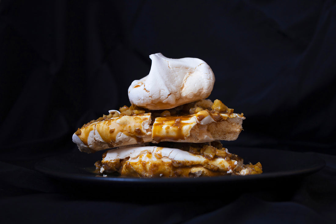 a piece of pavlova cake with walnuts and coffee sauce on a black background