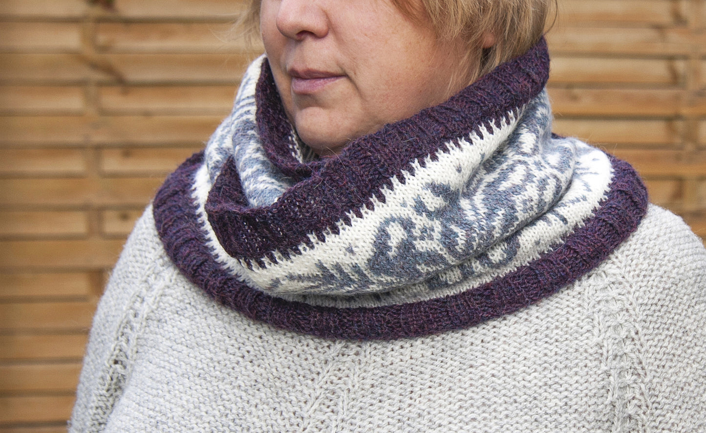 a woman performs hand-knitted Fair Isle cowl in Snowflake pattern made from purple and white alpaca wool yarn