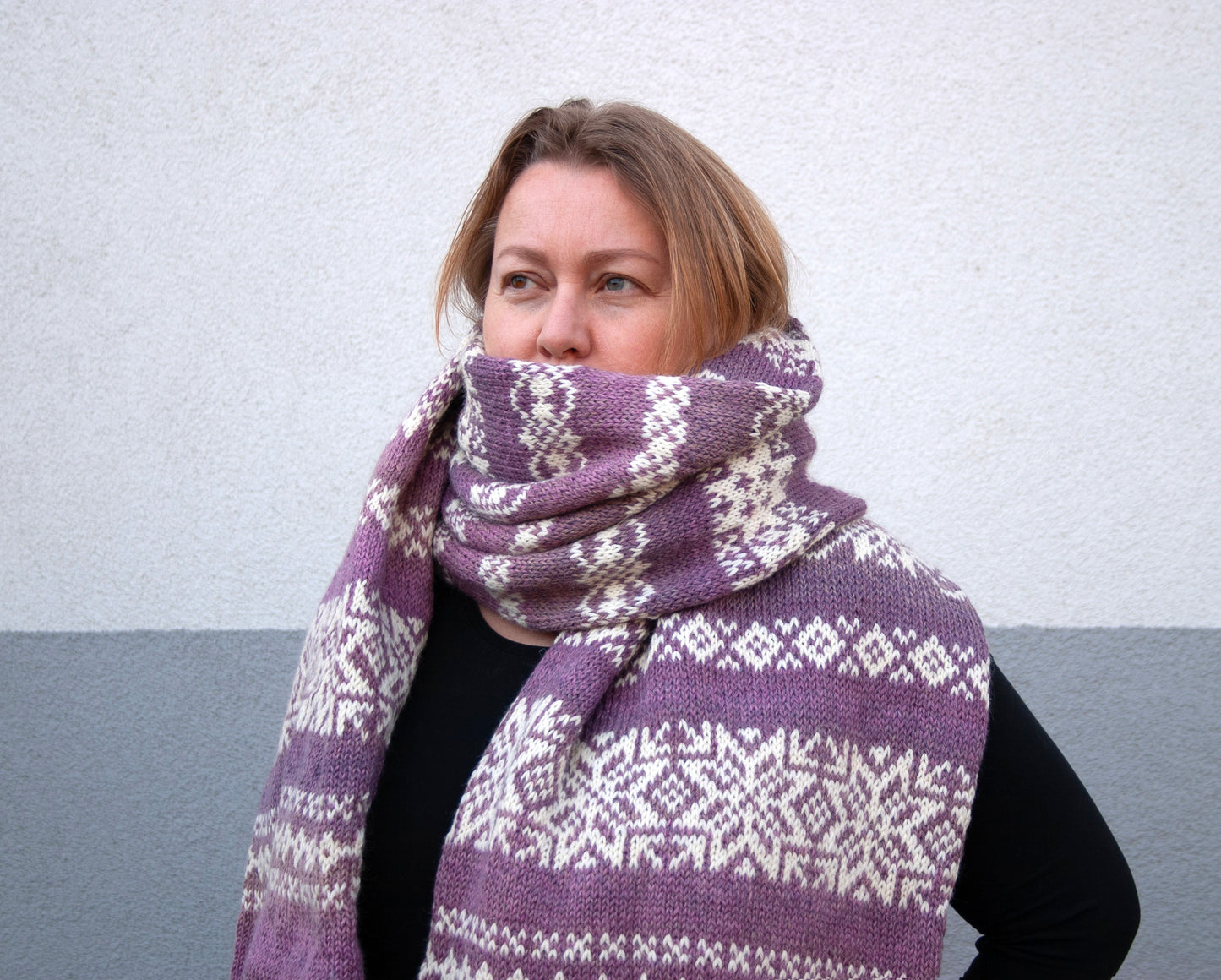 a woman performs long hand-knitted Fair Isle scarf made from gradient purple and white wool yarn
