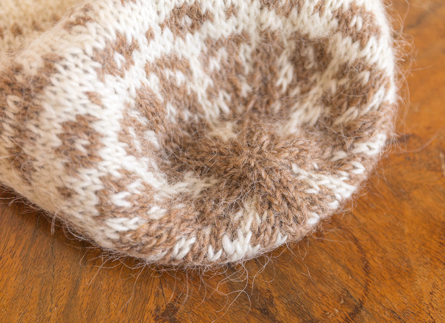 Close-up of a knitted beanie with brown and white pattern on a wooden surface