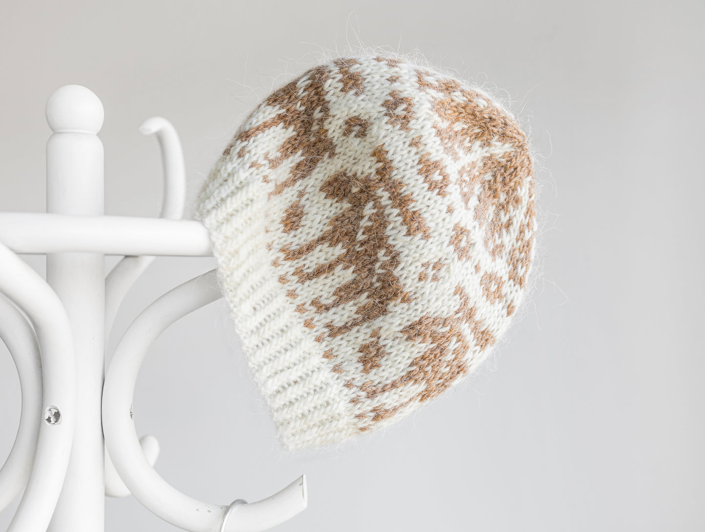 Knitted beanie with white and brown pattern features elk on a white stand against a light gray background