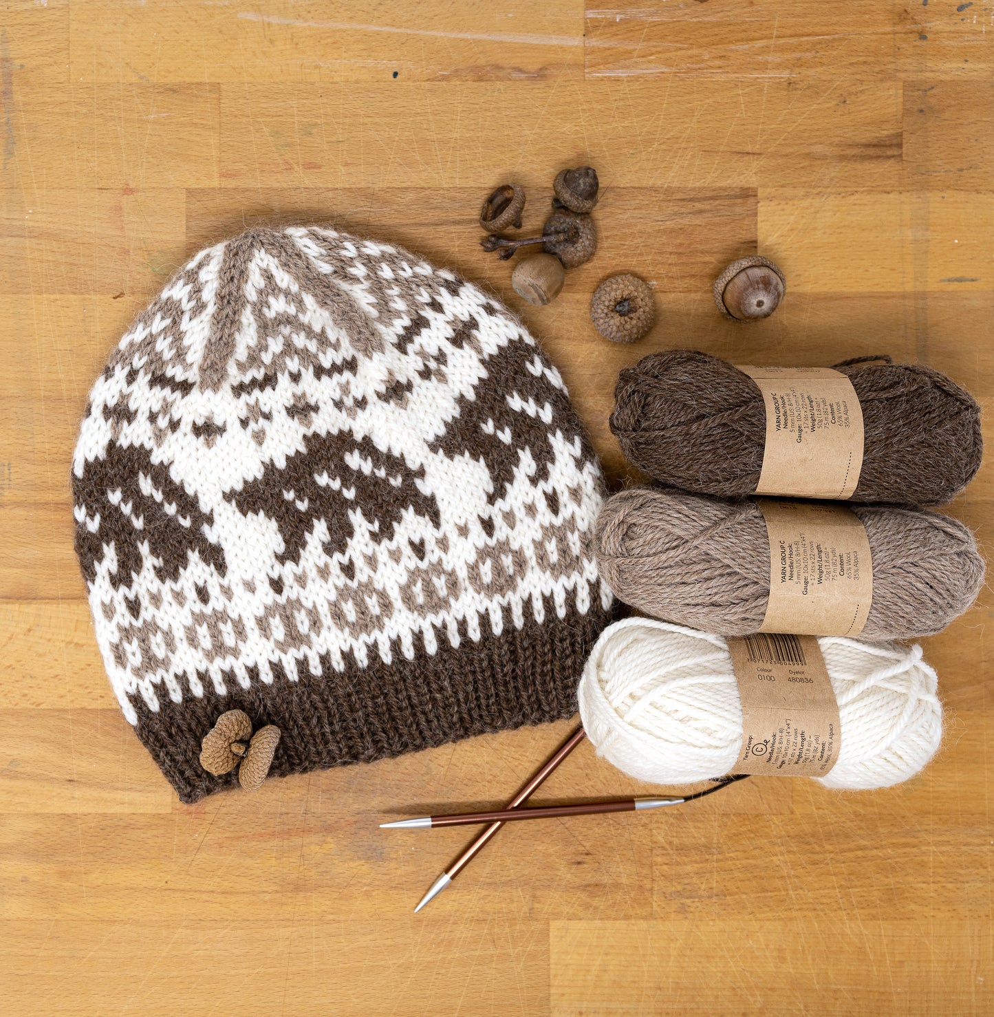 Knitted hat with bears pattern, yarn balls, and knitting needles on a wooden surface.