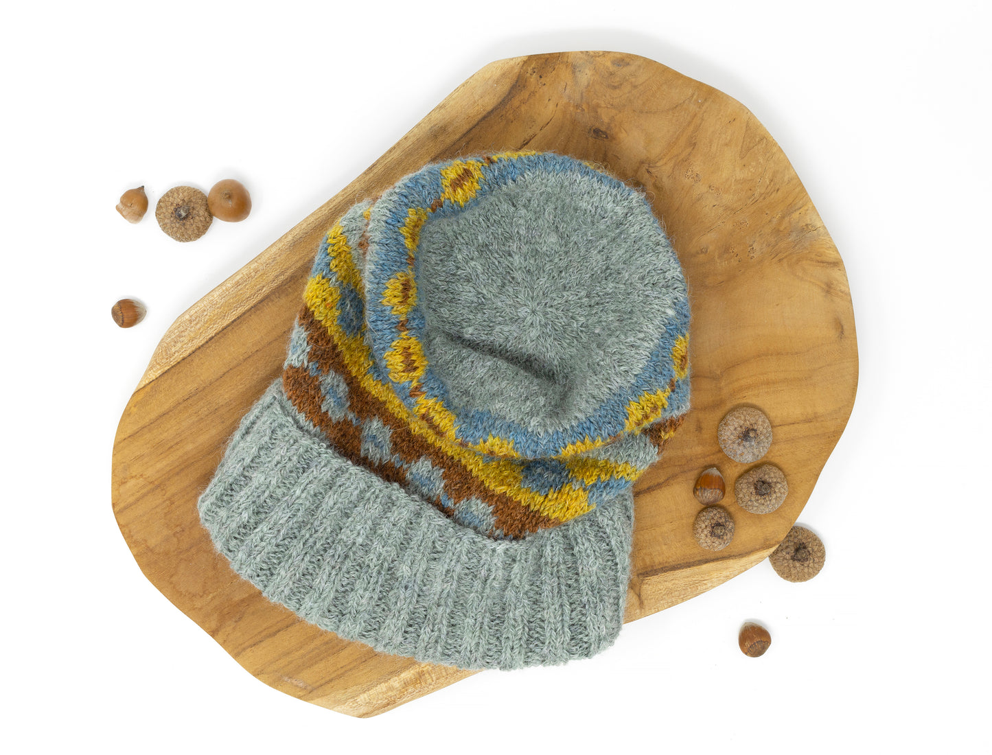 A crown of a grey, brown, yellow and blue alpaca wool hand-knitted Fair Isle hat displayed on a wooden background
