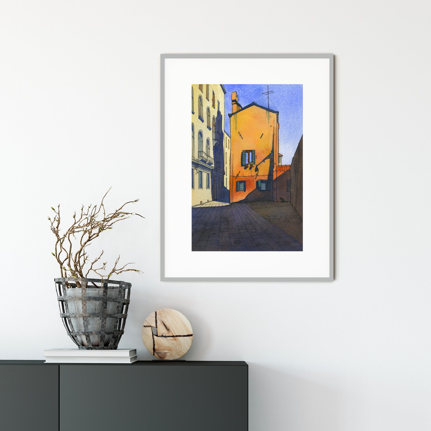 Framed watercolor and ink artwork of a city street scene in Cannaregio, Venice on a white wall with decorative items below.