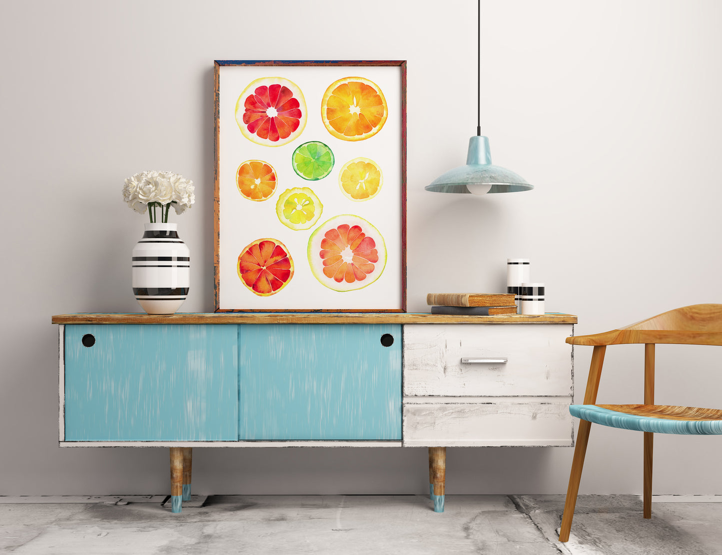A framed art print featuring colorful watercolor citrus slices chart hangs on a light gray wall above a mid-century modern sideboard.