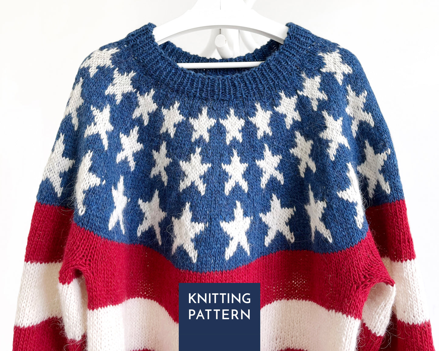 A knitted sweater with an American flag-inspired pattern, featuring a blue upper section with white stars, red and white horizontal stripes, and a dark blue label overlay reading 'KNITTING PATTERN'