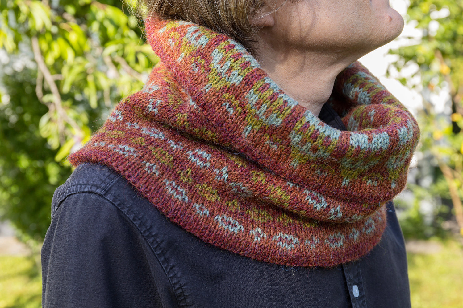 Man performs a woll cowl in brick red and green colours
