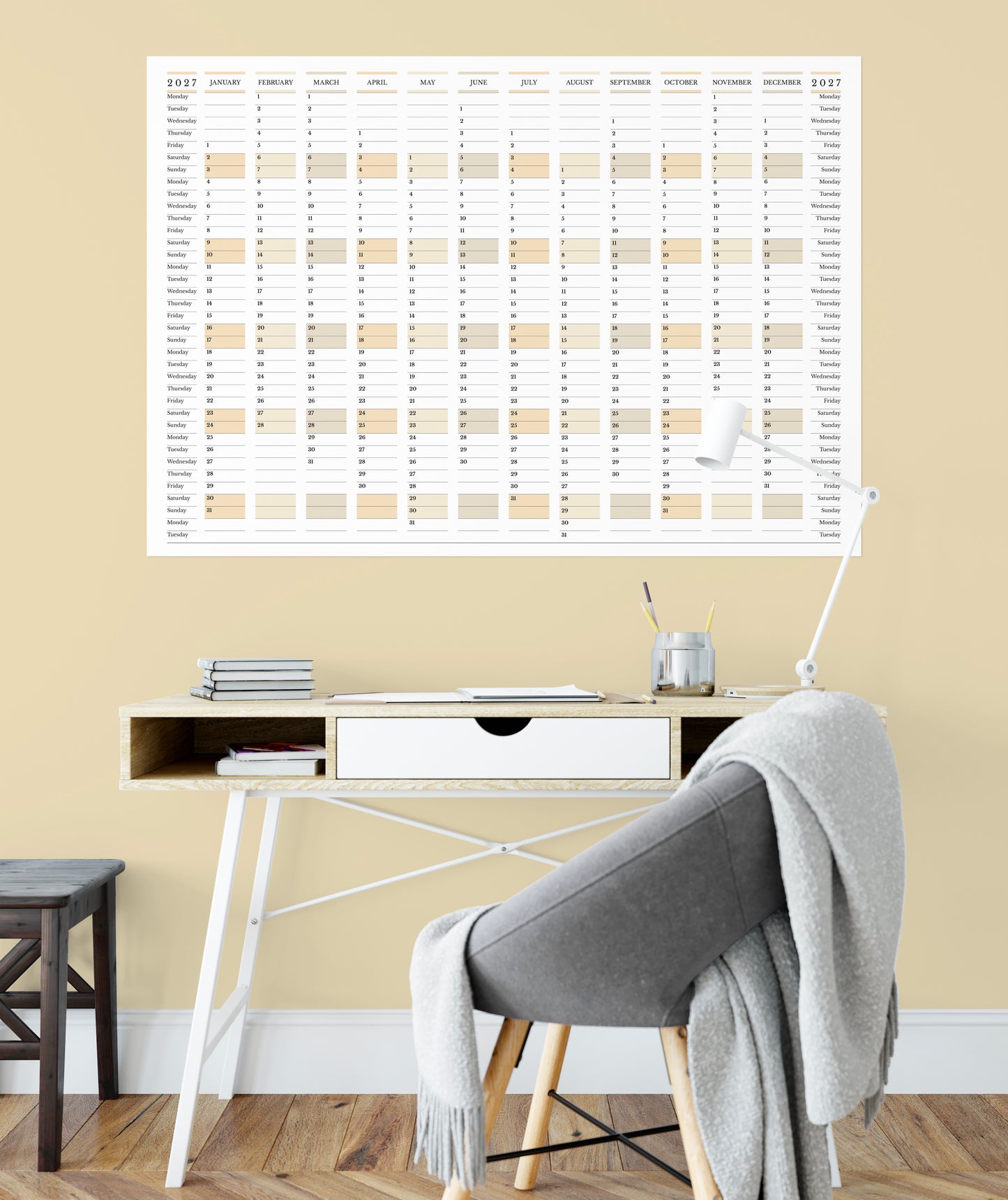 2027 minimal yearly planner, Monday start, landscape orientation, on a beige wall above a desk with office furniture.