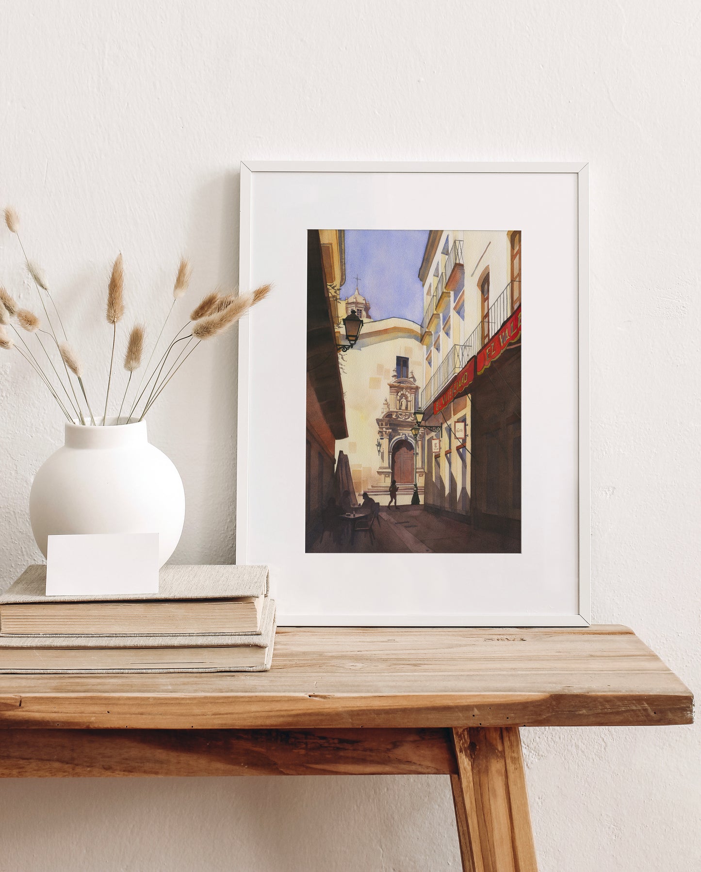 Framed watercolor artwork of a street scene in Old town of Almeria, Spain, on a wooden table with decorative items