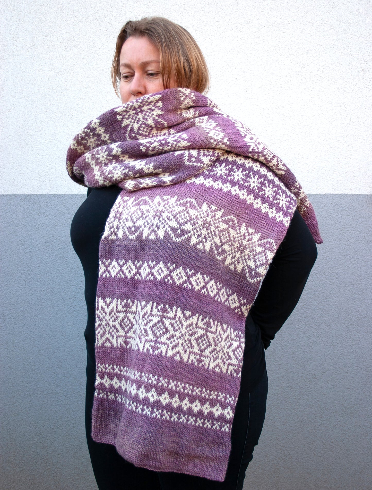 a woman performs long hand-knitted Fair Isle scarf made from gradient purple and white wool yarn