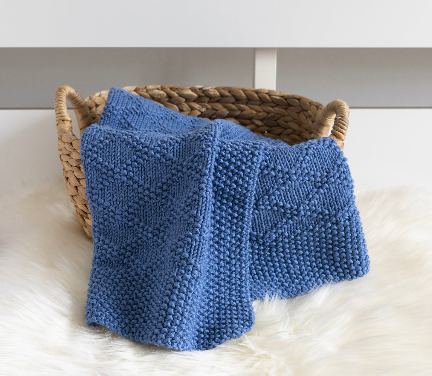 Blue merino wool hand-knitted blanket in Charles Brocade pattern in a basket