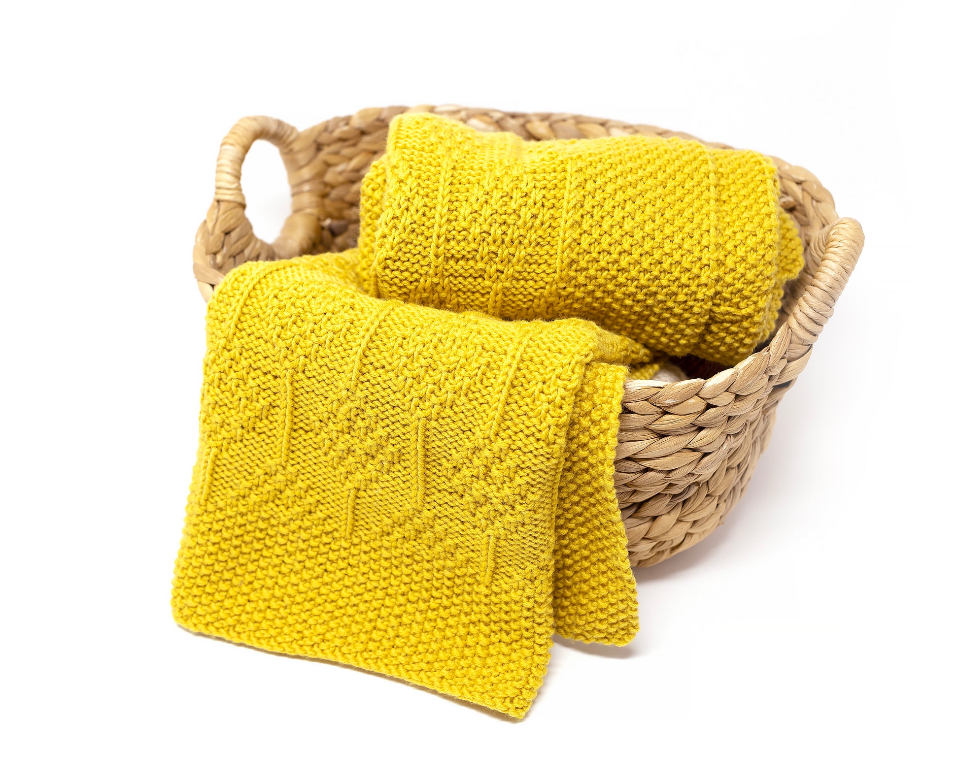 A bright mustrad yellow knitted blanket in diamonds texture displayed in a woven natural fiber basket on a white background.