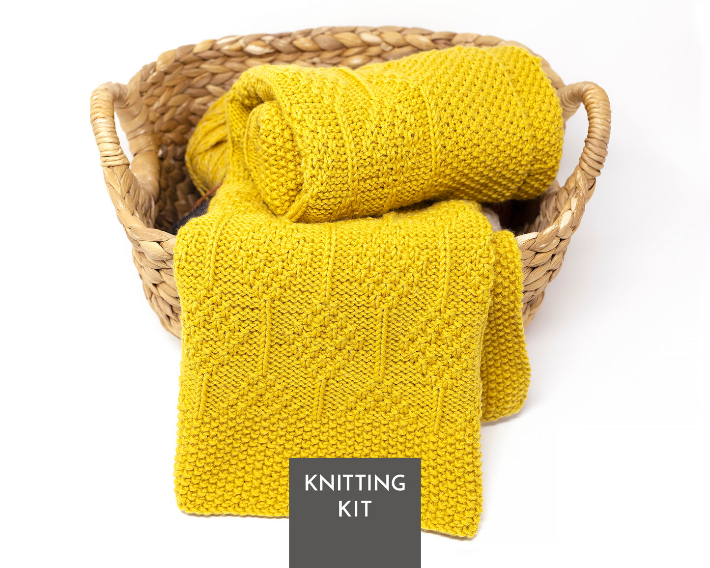 A yellow knitted blanket displayed in a woven straw basket on a white background, with a dark gray label reading 'KNITTING KIT' at the bottom.