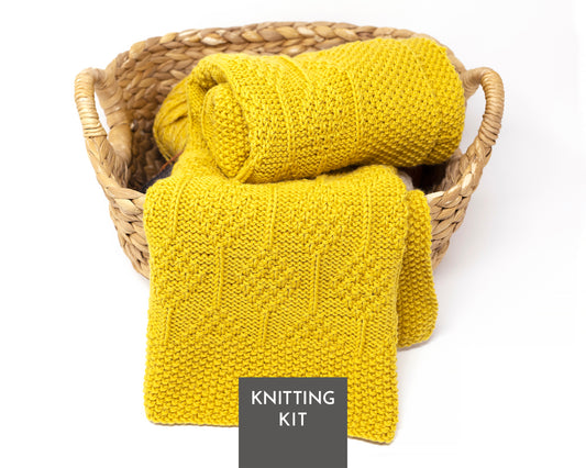 A yellow knitted blanket with diamonds pattern displayed in a woven straw basket on a white background, with a dark gray label reading 'KNITTING KIT' at the bottom.