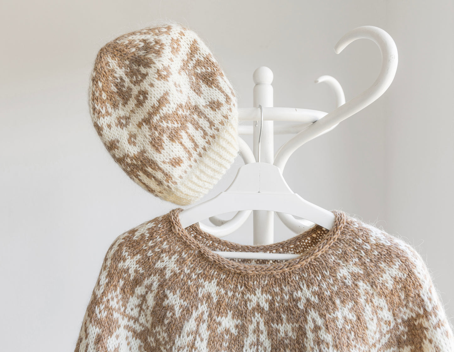 Knitted sweater and hat with a white coat rack on a light gray background