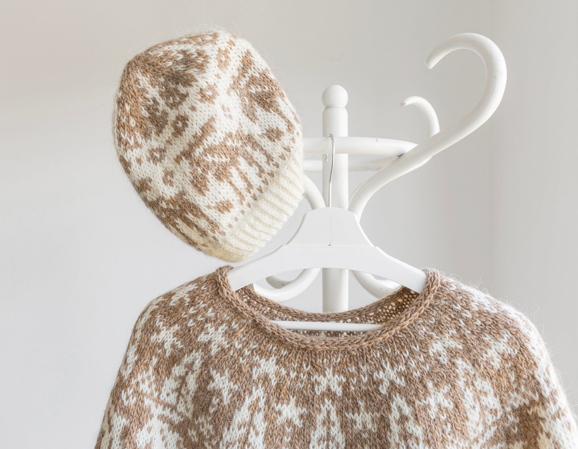Knitted sweater and hat with a white coat rack on a light gray background