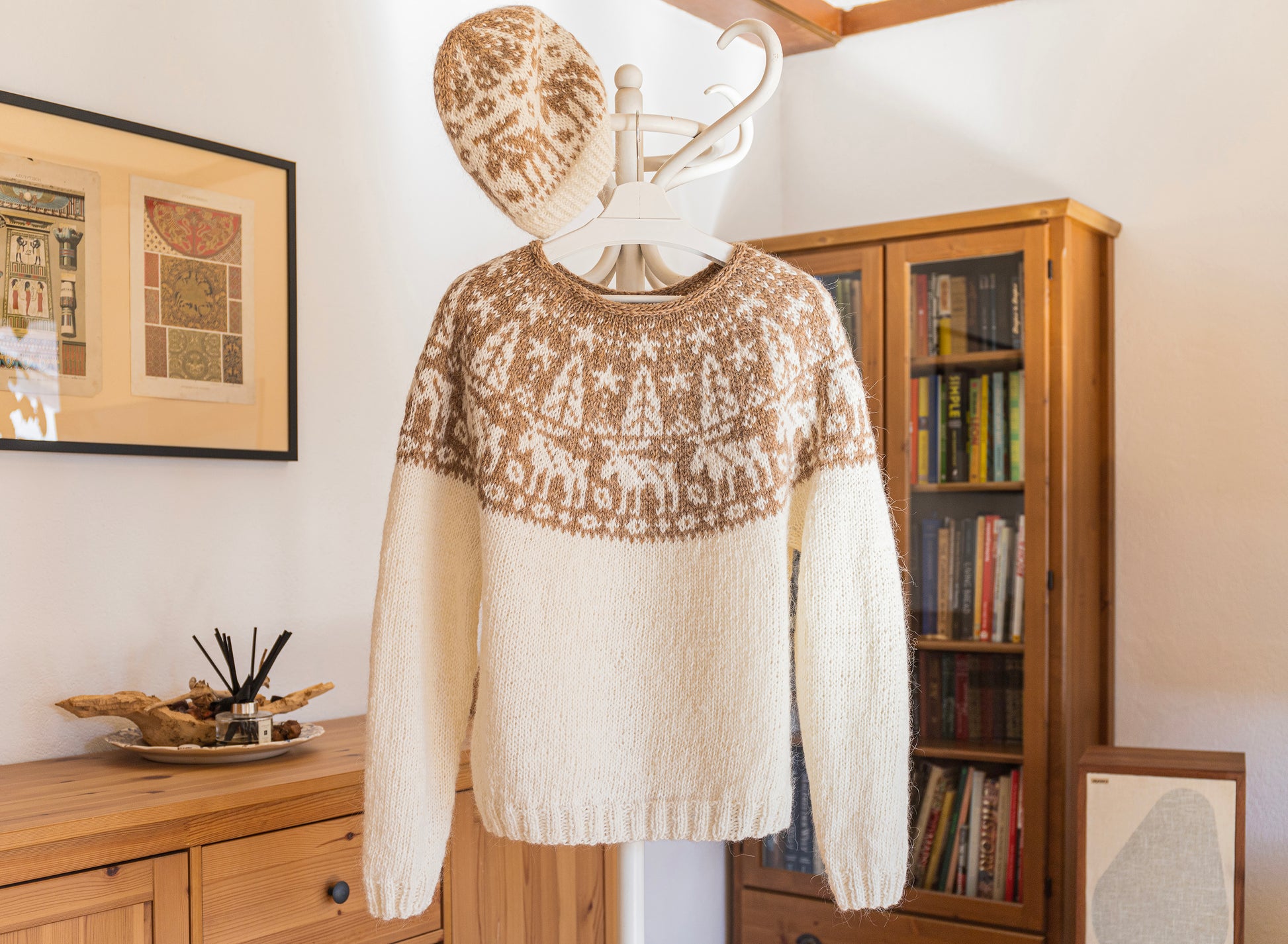 White sweater with brown pattern and matching hat on a mannequin against a home interior background