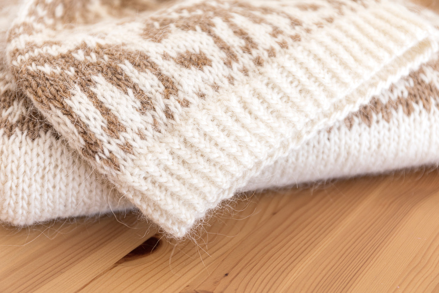 Close-up of a knitted hat with brown and white pattern on a wooden surface