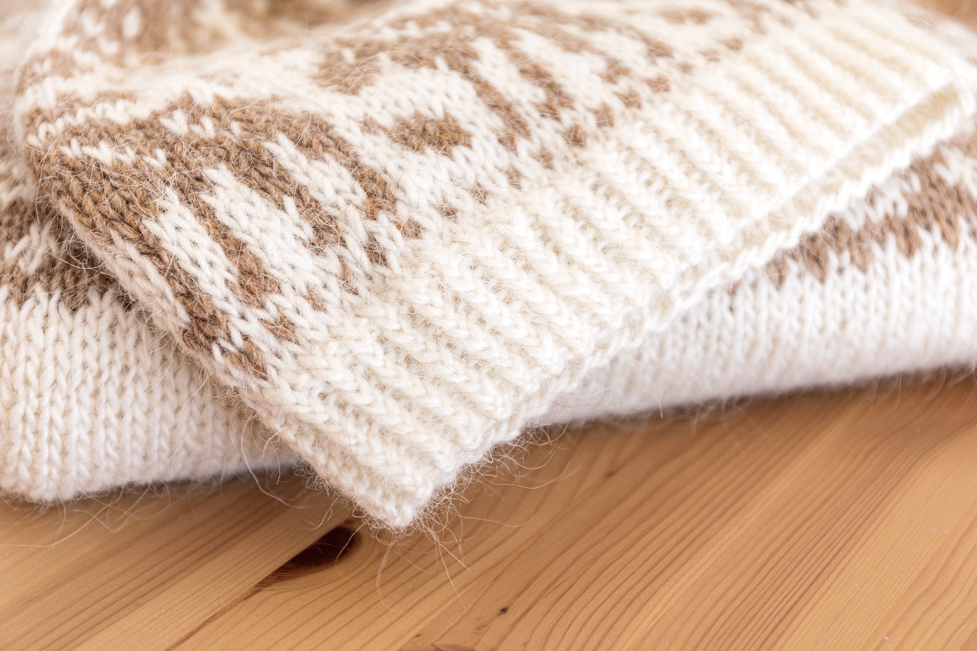Close-up of a knitted hat with brown and white pattern on a wooden surface