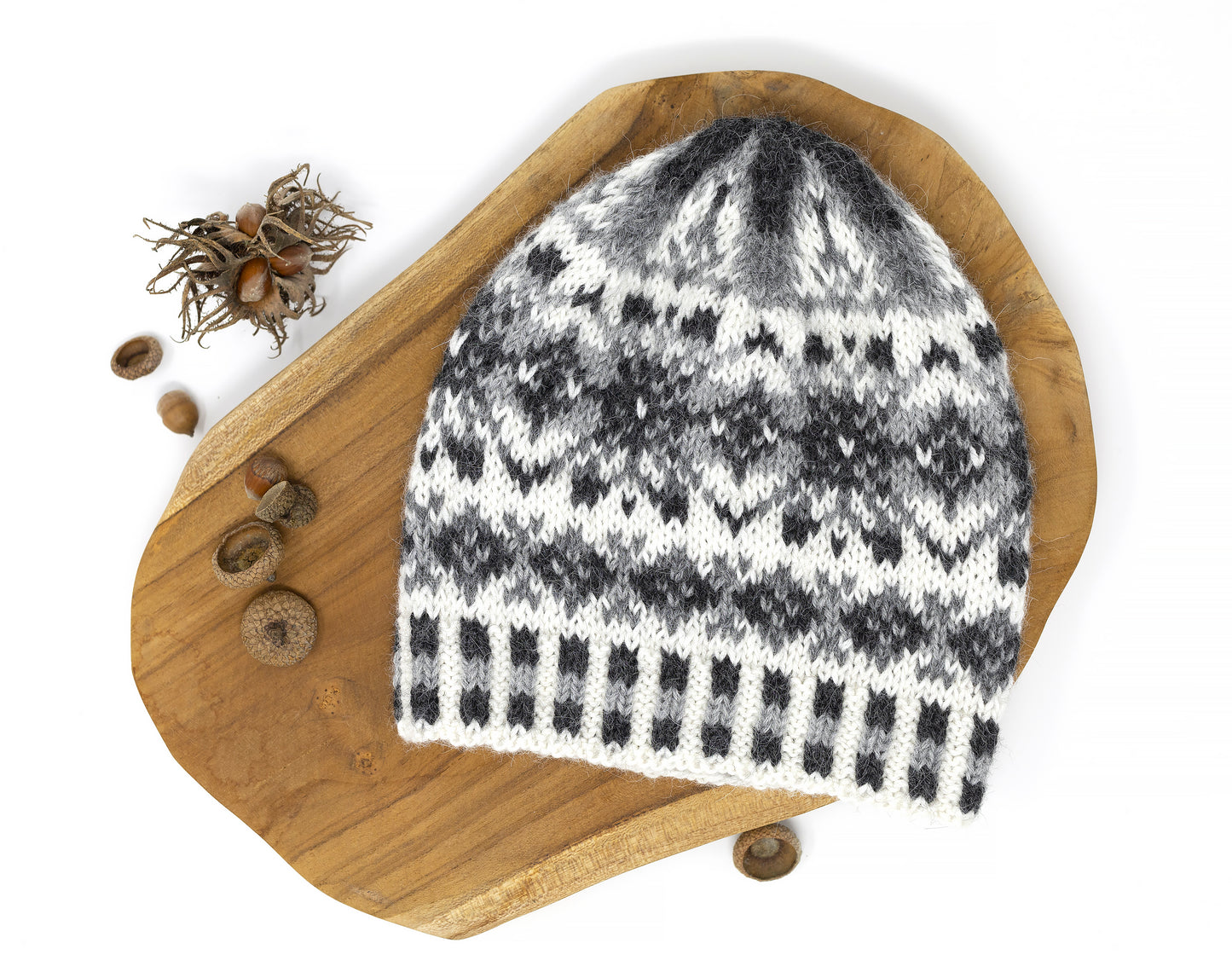 Front view of a rey, white and black alpaca wool hand-knitted Fair Isle hat displayed on a wooden board