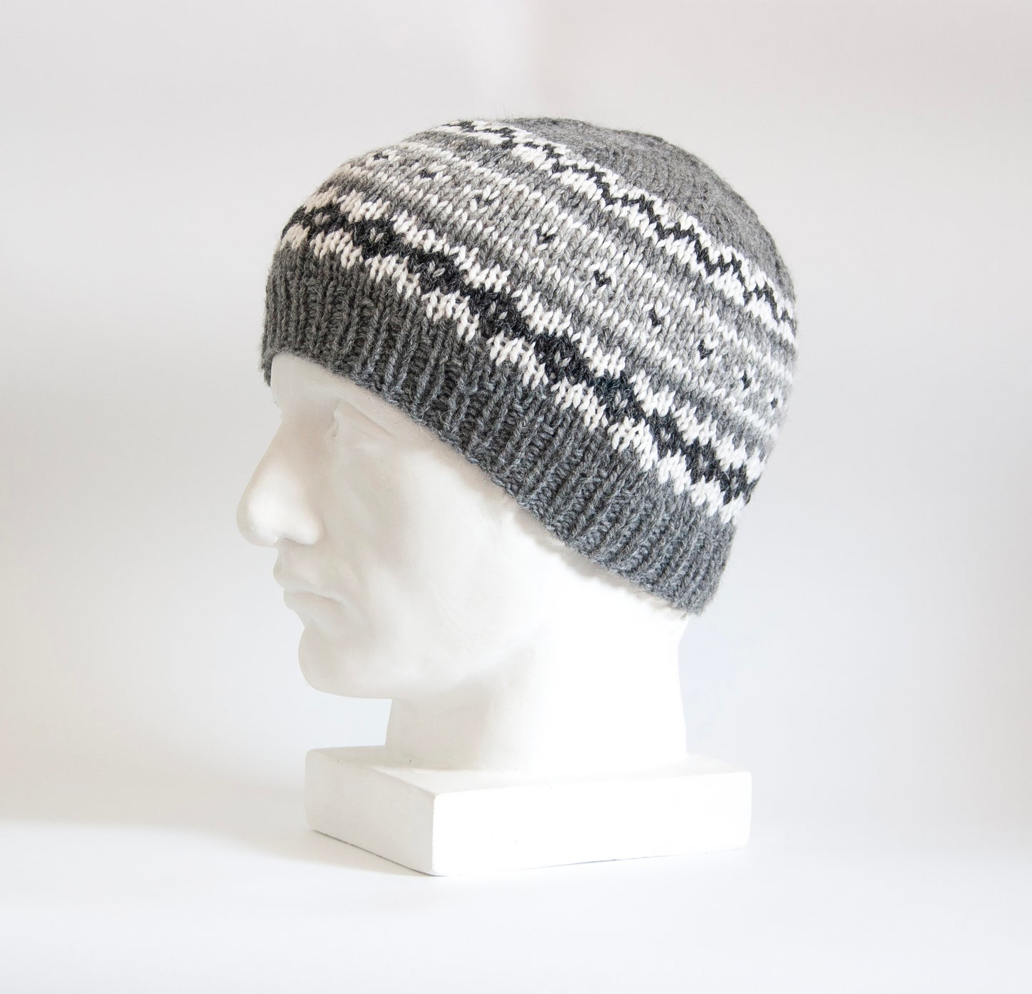 Gray and white hand-knitted Fair Isle beanie hat displayed on a white plaster bust.