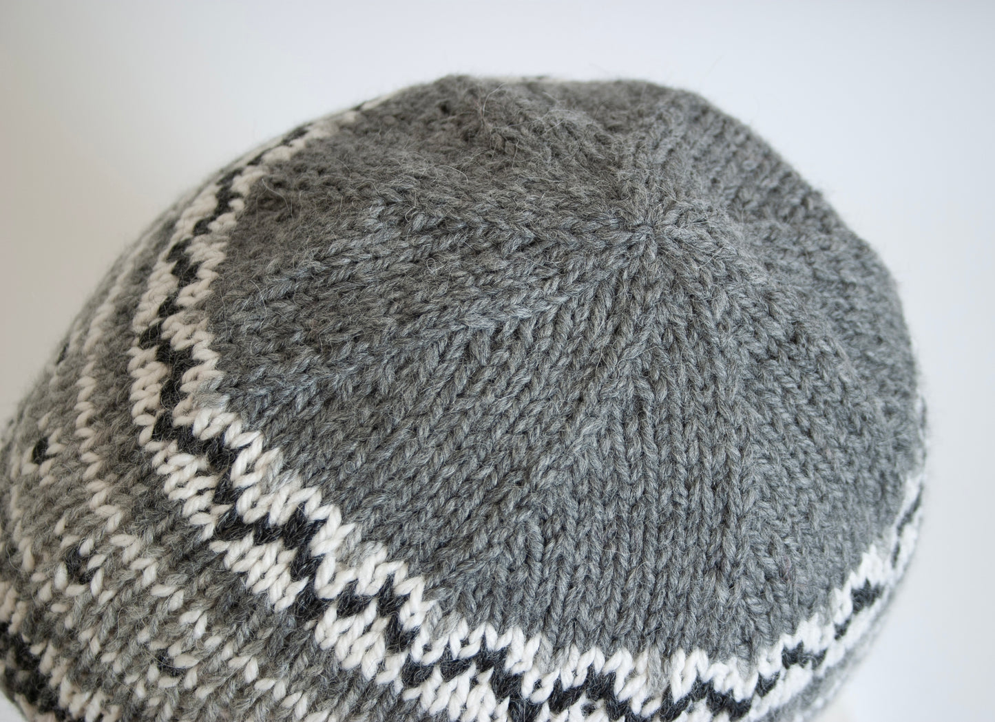 Close up for a crown of a gray and white hand-knitted Fair Isle beanie hat 