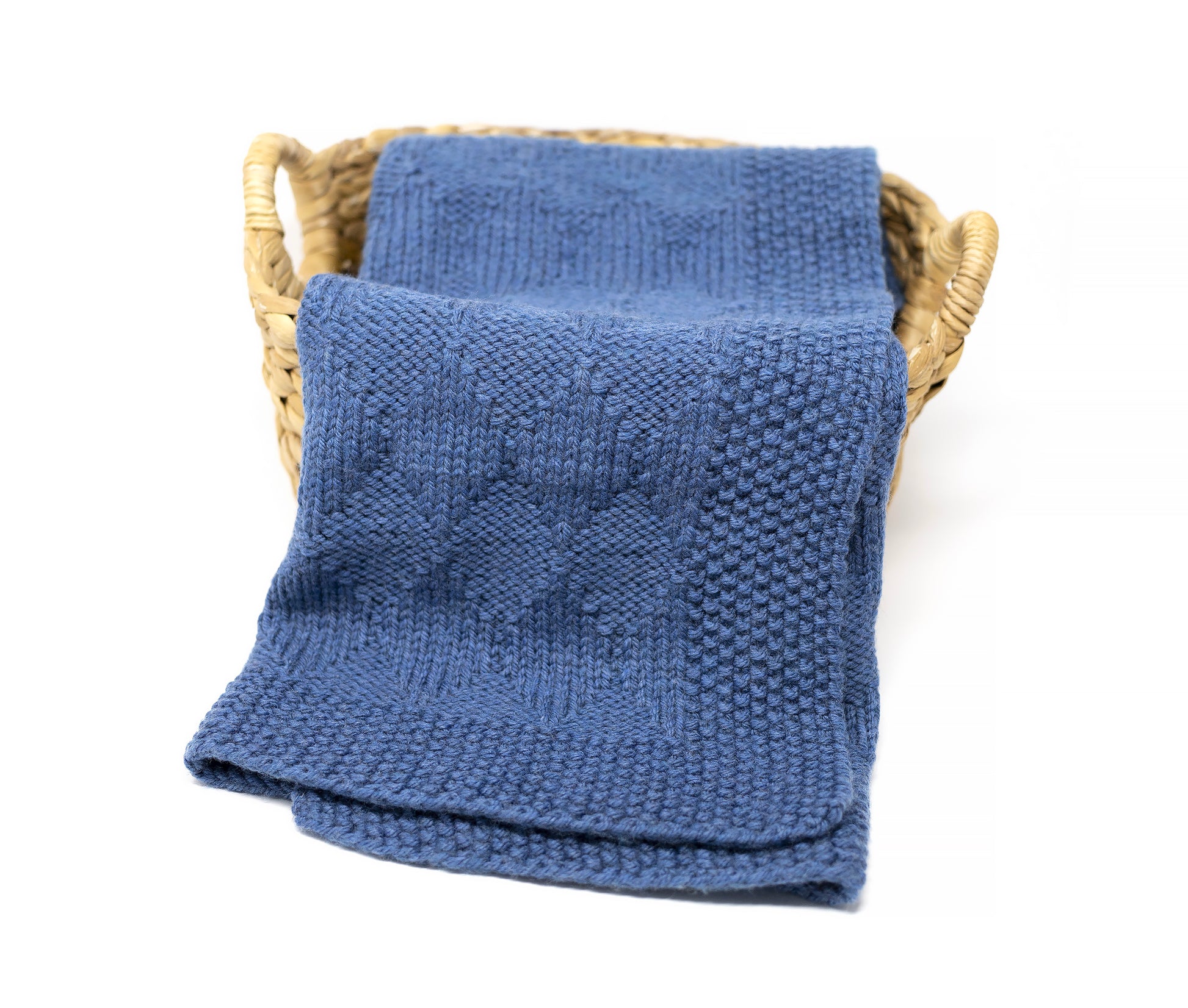 A folded blue knitted Harlequin blanket with a textured diamonds pattern, displayed inside a light brown woven basket on a white background.