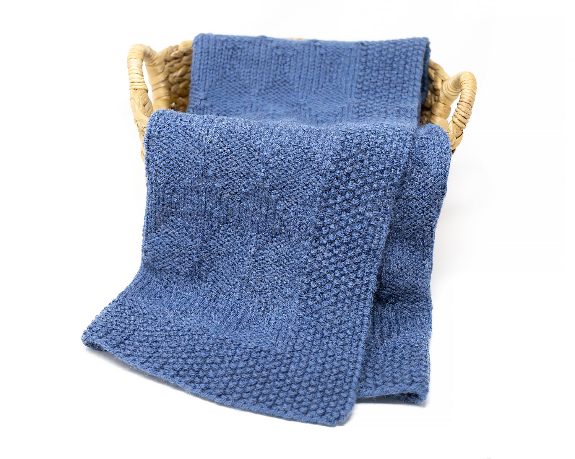 Blue textured knitted blanket draped over a woven basket on a white background