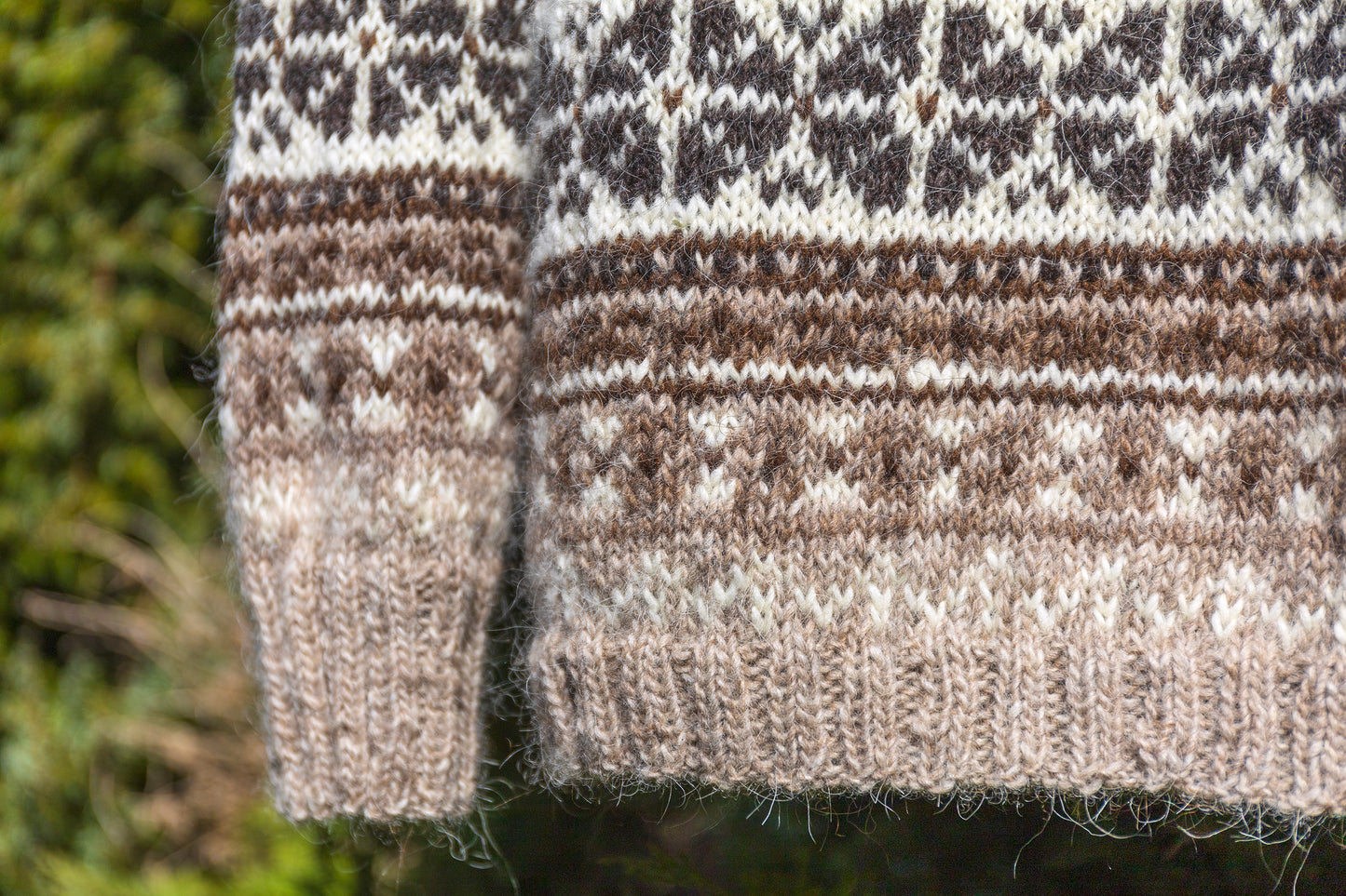 Close-up of Helga lopapeysa sweater hems with a border pattern against a blurred natural background