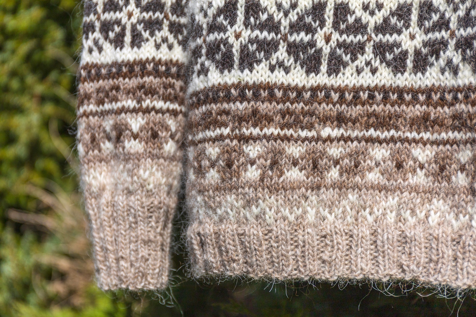 Close-up of Helga lopapeysa sweater hems with a border pattern against a blurred natural background