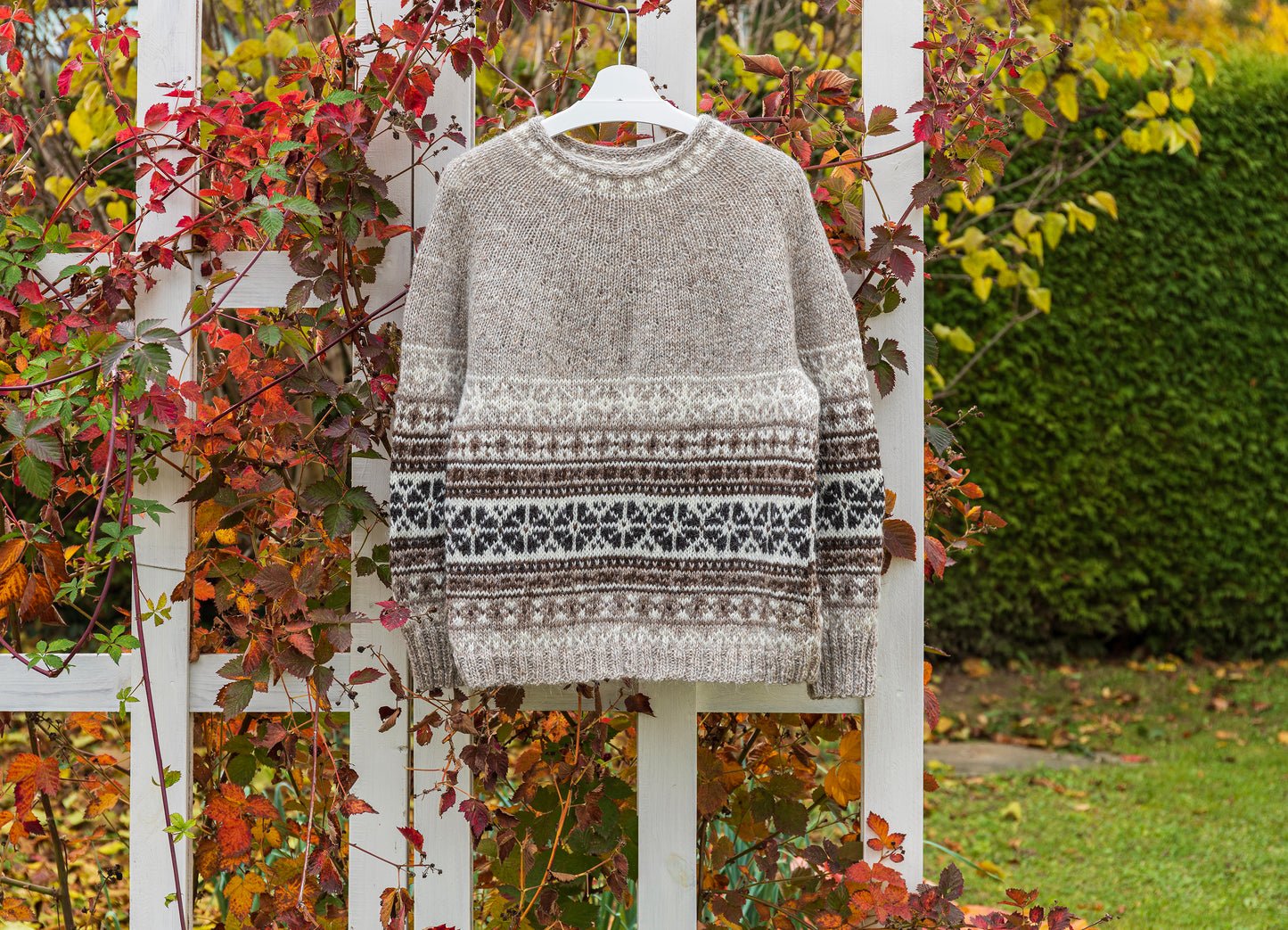 Helga icelandic sweater on a fence against a natural background with greenery and autumn leaves.