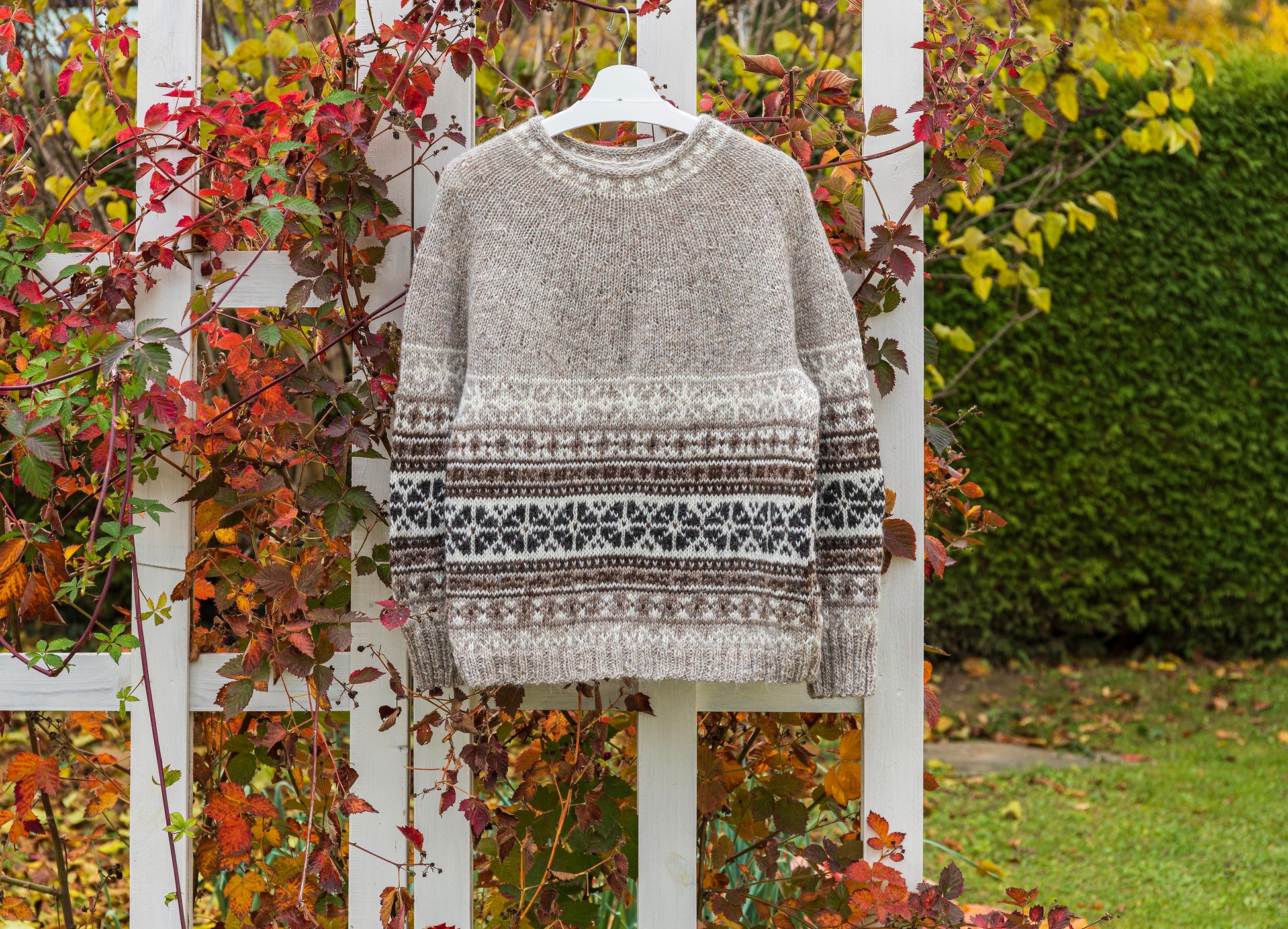 Helga icelandic sweater on a fence against a natural background with greenery and autumn leaves.