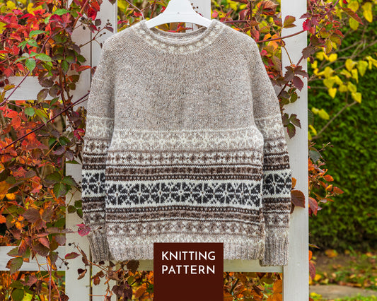 A knitted sweater with a Fair Isle pattern in brown, white, and black, hanging on a white hanger against a white fence with autumn foliage. A brown label at the bottom reads 'KNITTING PATTERN'.