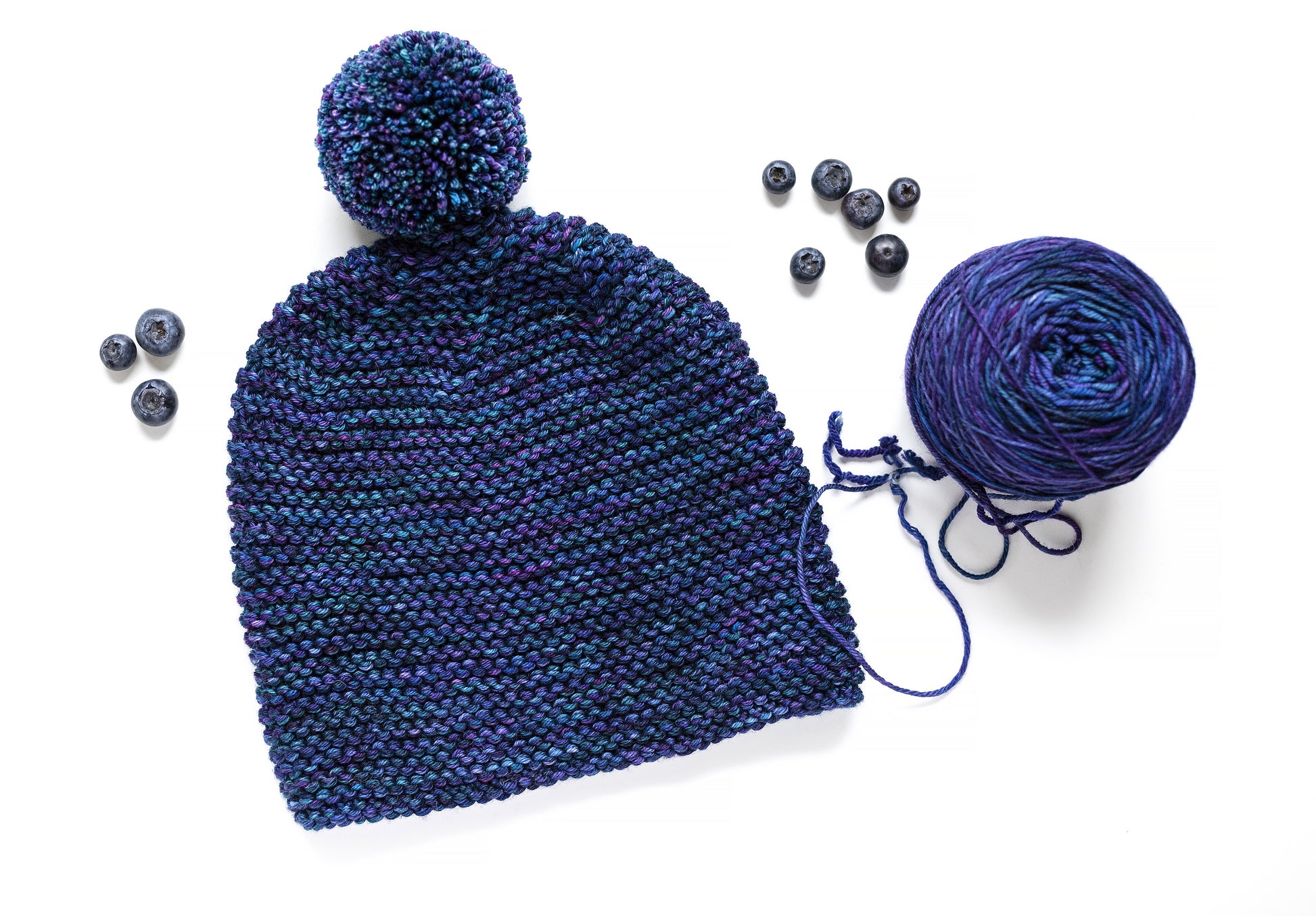 blue and purple gradient wool garter stitch hand-knitted pom pom hat with yarn ball