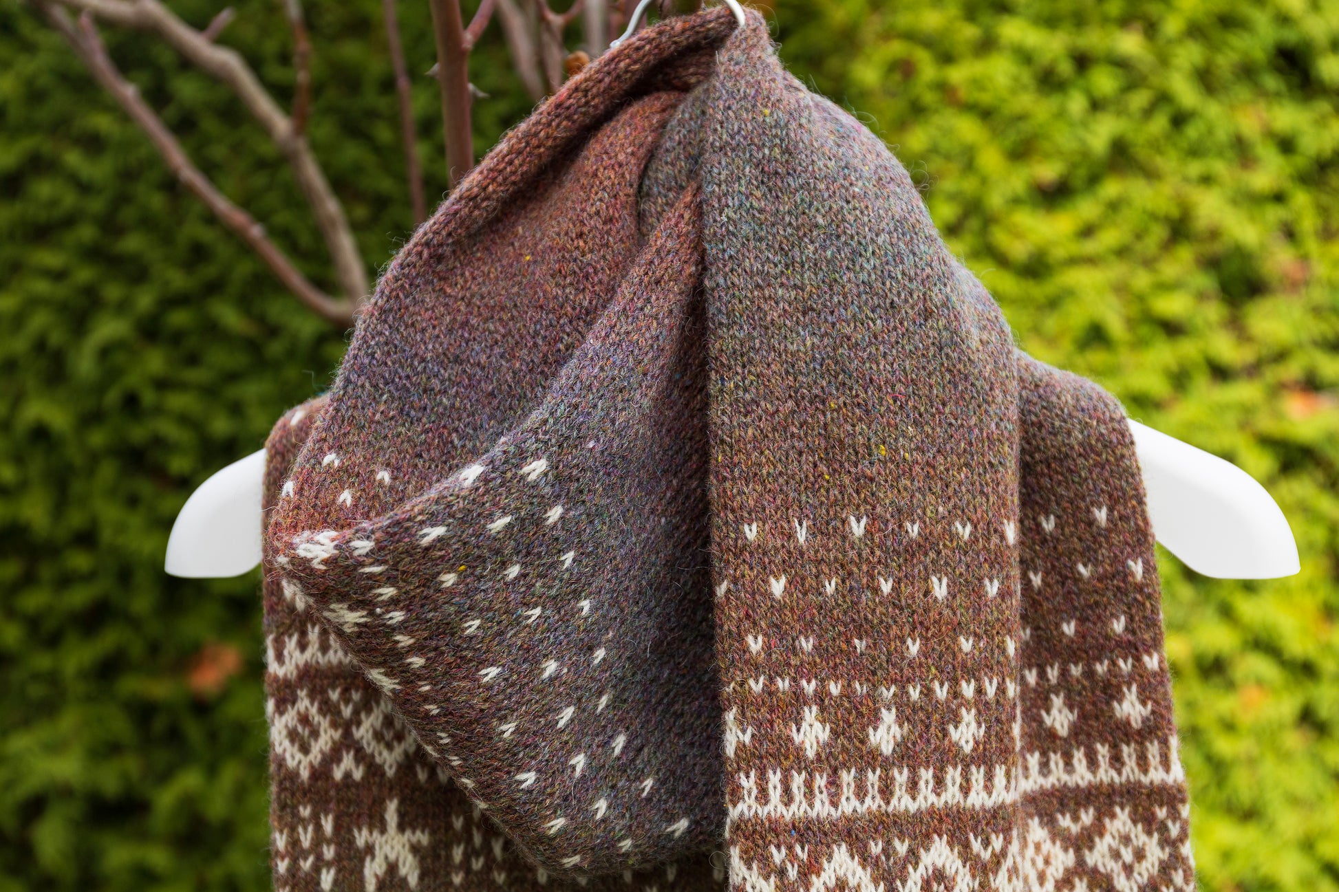 Close-up of hand-knitted Lahemaa Squirrel Fair Isle scarf draped over a mannequin against a green background