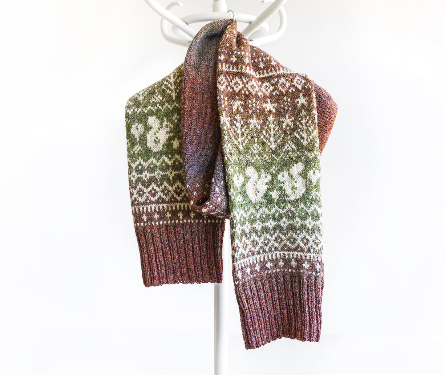 Knitted scarf with green and brown gradient pattern with squirrels and trees on a white background