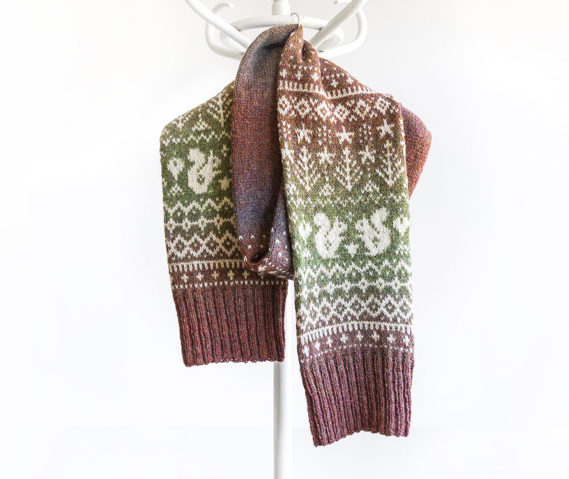 Knitted scarf with green and brown gradient pattern with squirrels and trees on a white background