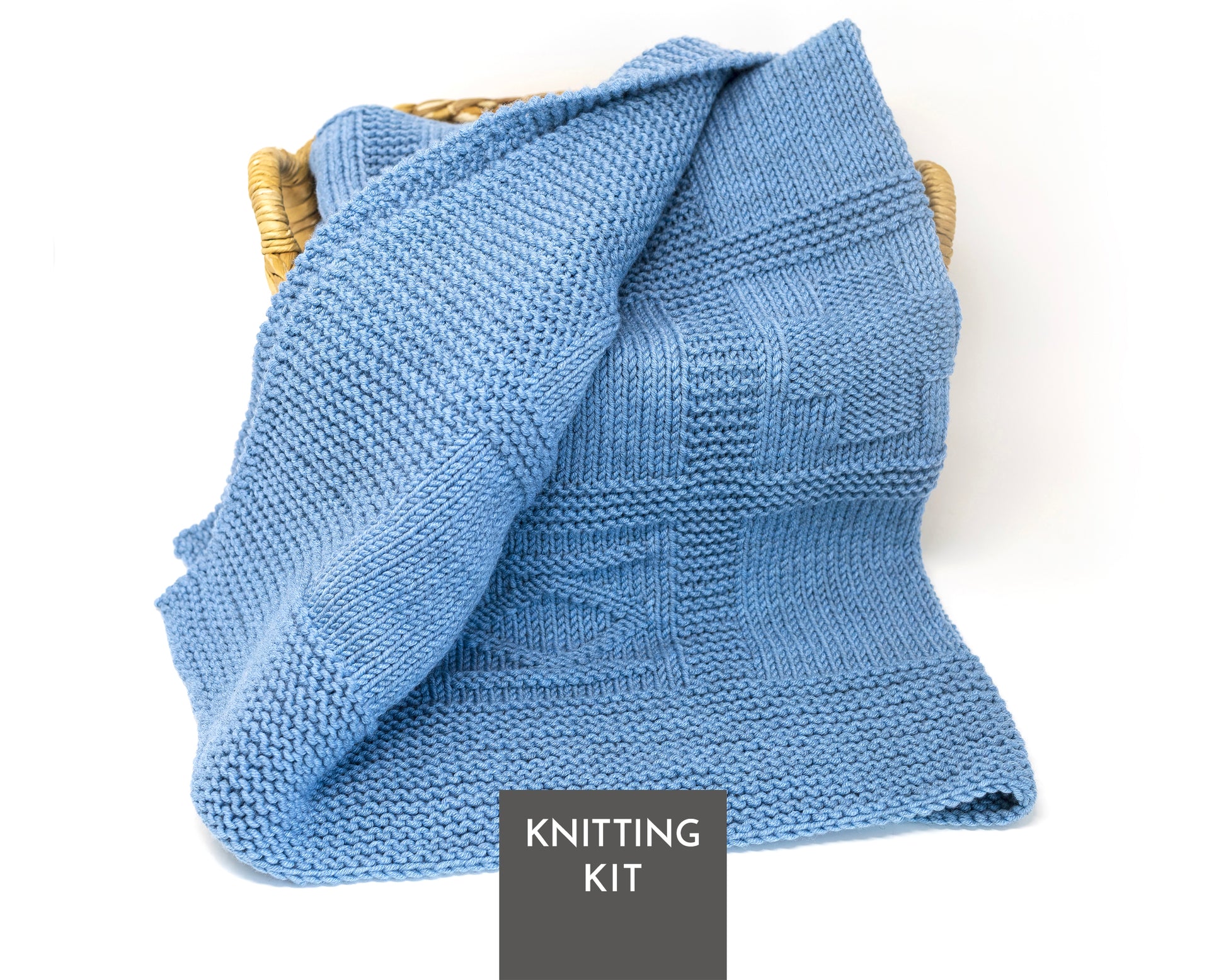 A light blue knitted blanket draped over a woven basket, with a dark gray label at the bottom reading 'KNITTING KIT'.