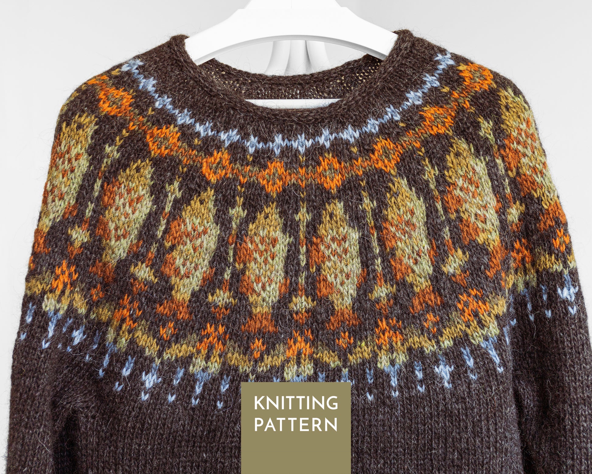 A close-up of a knitted sweater with a Fair Isle fish pattern in brown, orange, beige, and light blue, hanging on a white hanger against a light gray background. A label at the bottom reads 'KNITTING PATTERN'.