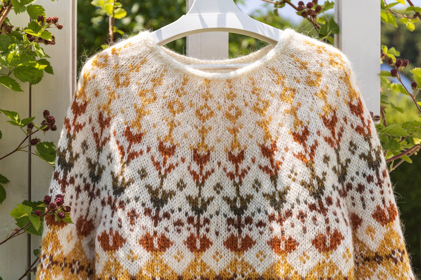 close-up of Meadow icelandic lopapeysa sweater with a floral pattern on a hanger against a natural background