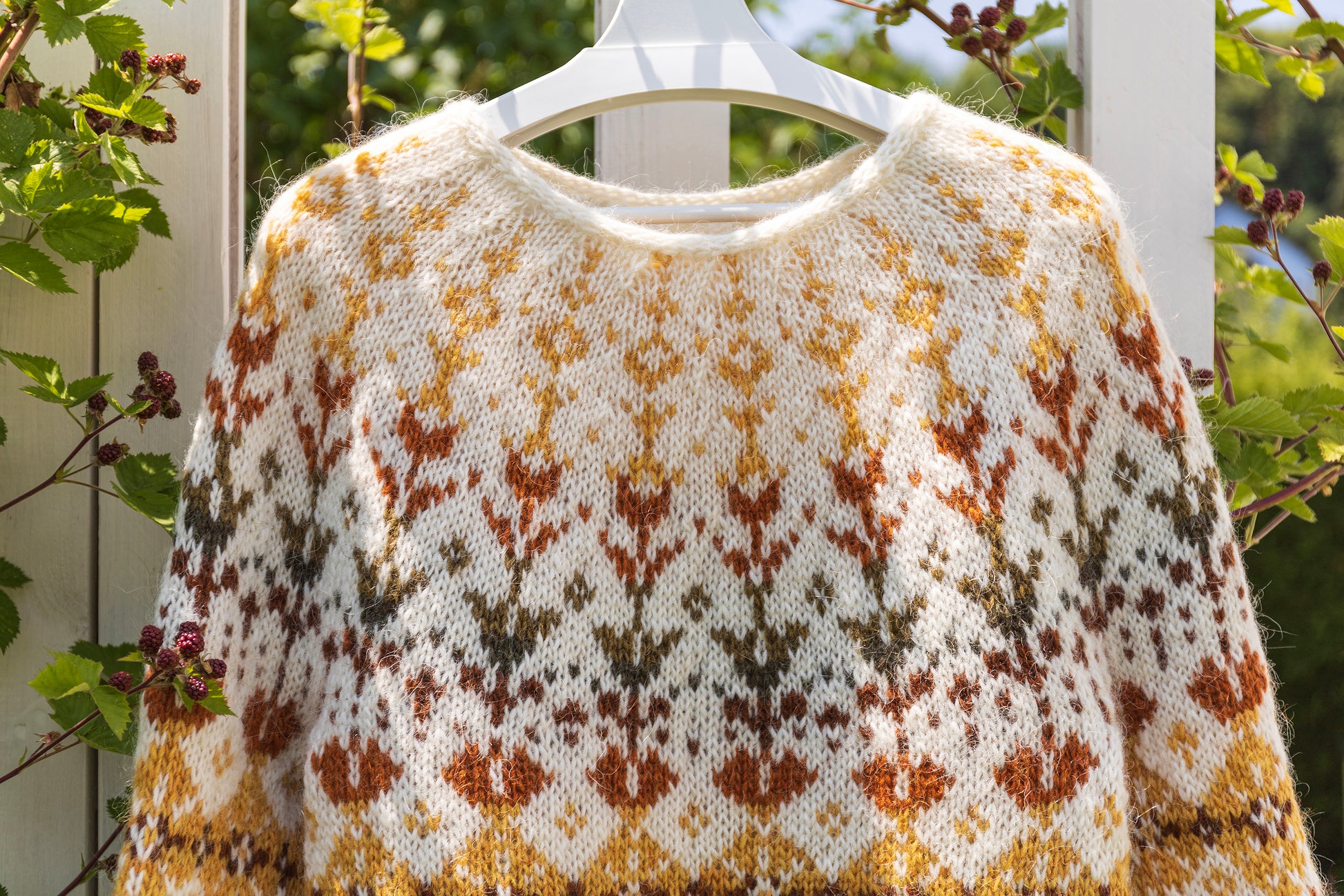 close-up of Meadow icelandic lopapeysa sweater with a floral pattern on a hanger against a natural background