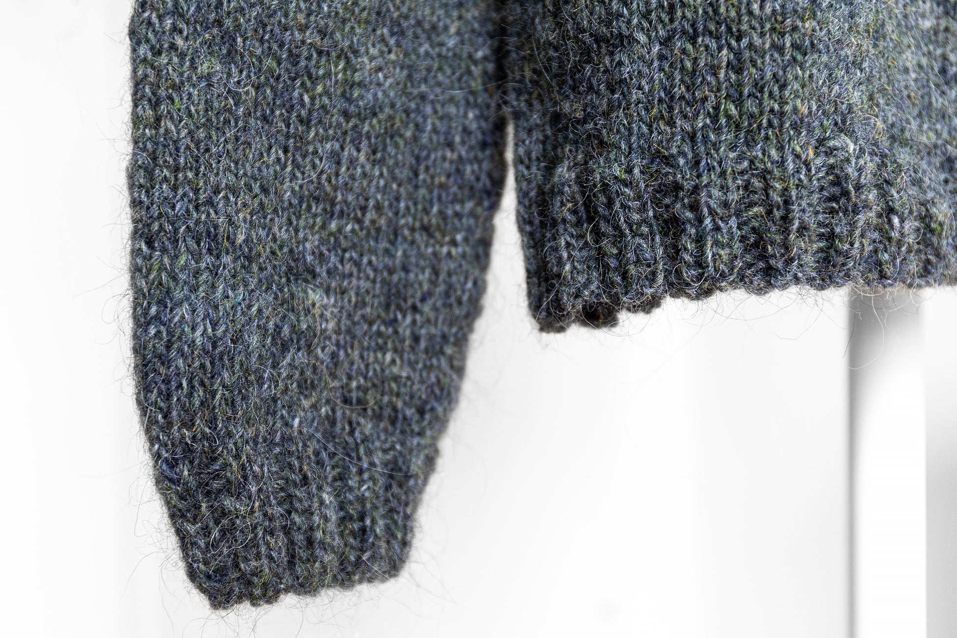 Close-up of a hem and a cuff of gray knitted sweater on a white background