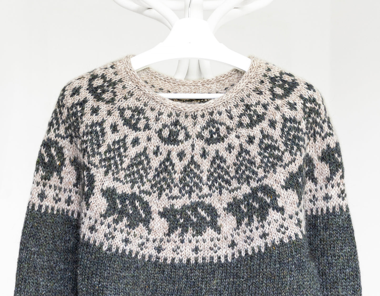 Hand-knitted sweater with a bears and trees motif pattern on a hanger against a white background 