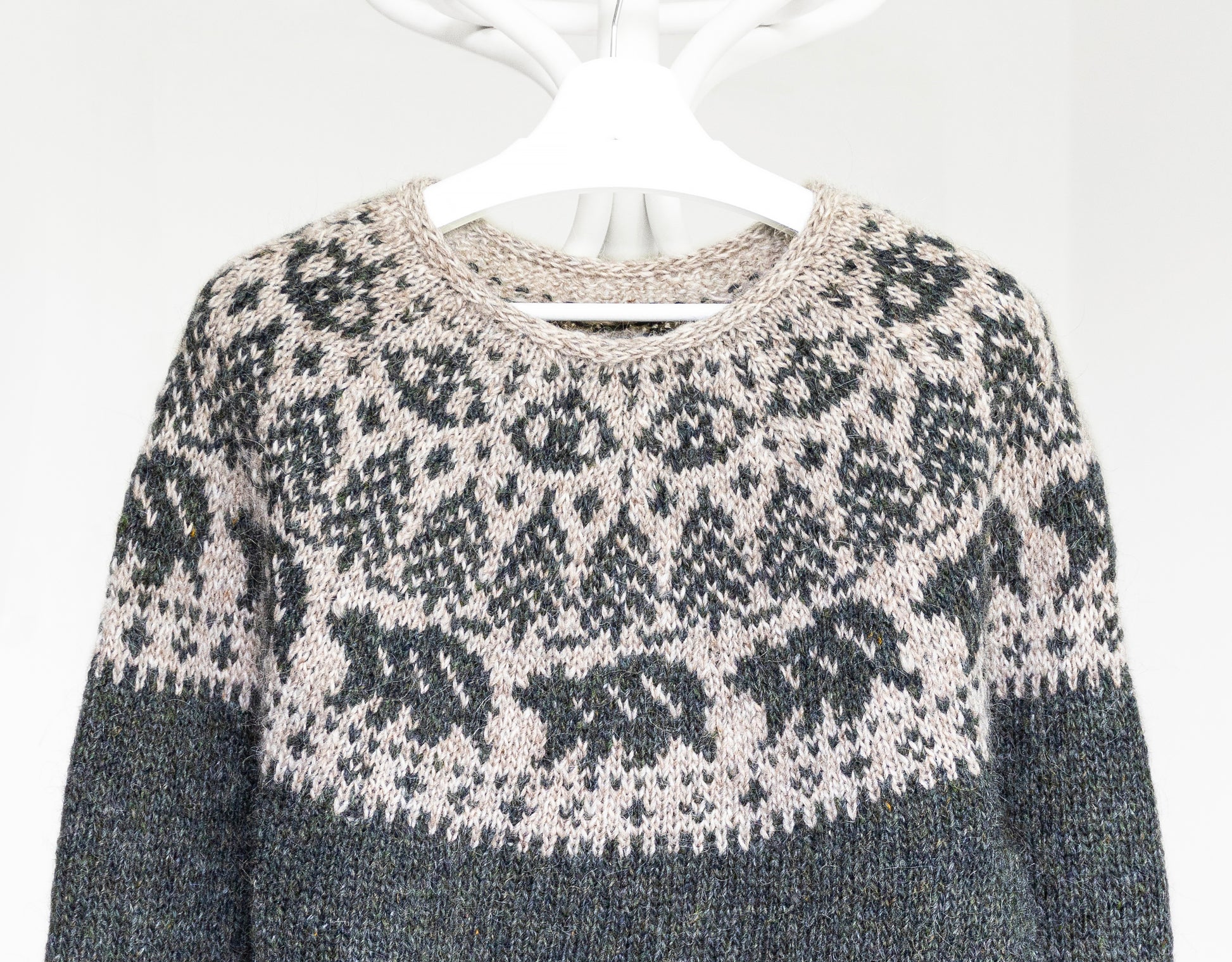 Hand-knitted sweater with a bears and trees motif pattern on a hanger against a white background 