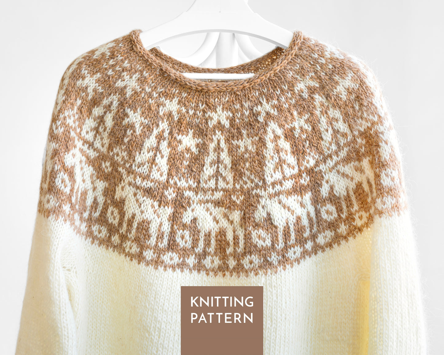 A close-up of a knitted sweater on a white hanger, showing a cream and brown Moose Fair Isle pattern across the yoke with solid cream sleeves. A brown label at the bottom reads 'KNITTING PATTERN'.