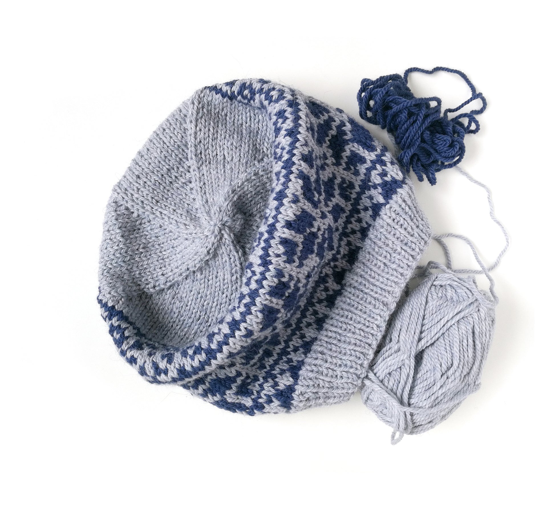 grey and blue wool hand-knitted Fair Isle beanie hat in Roses knitting pattern with yarn skeins