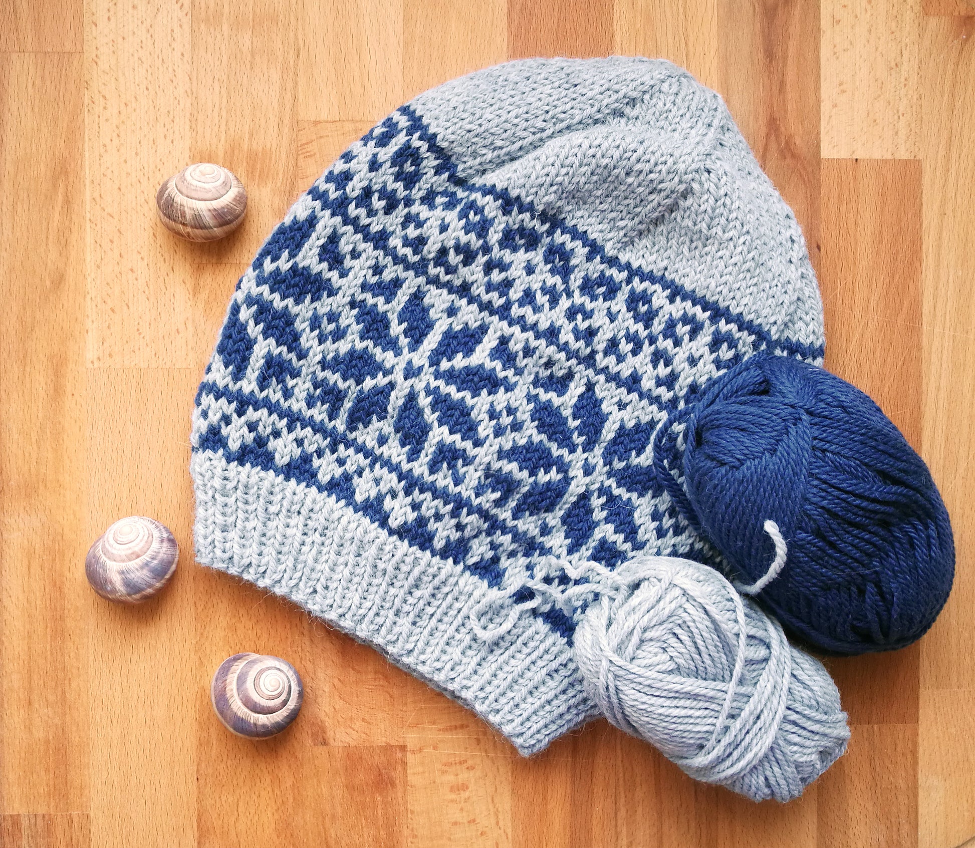grey and blue wool hand-knitted Fair Isle beanie hat in Roses knitting pattern on a wooden background