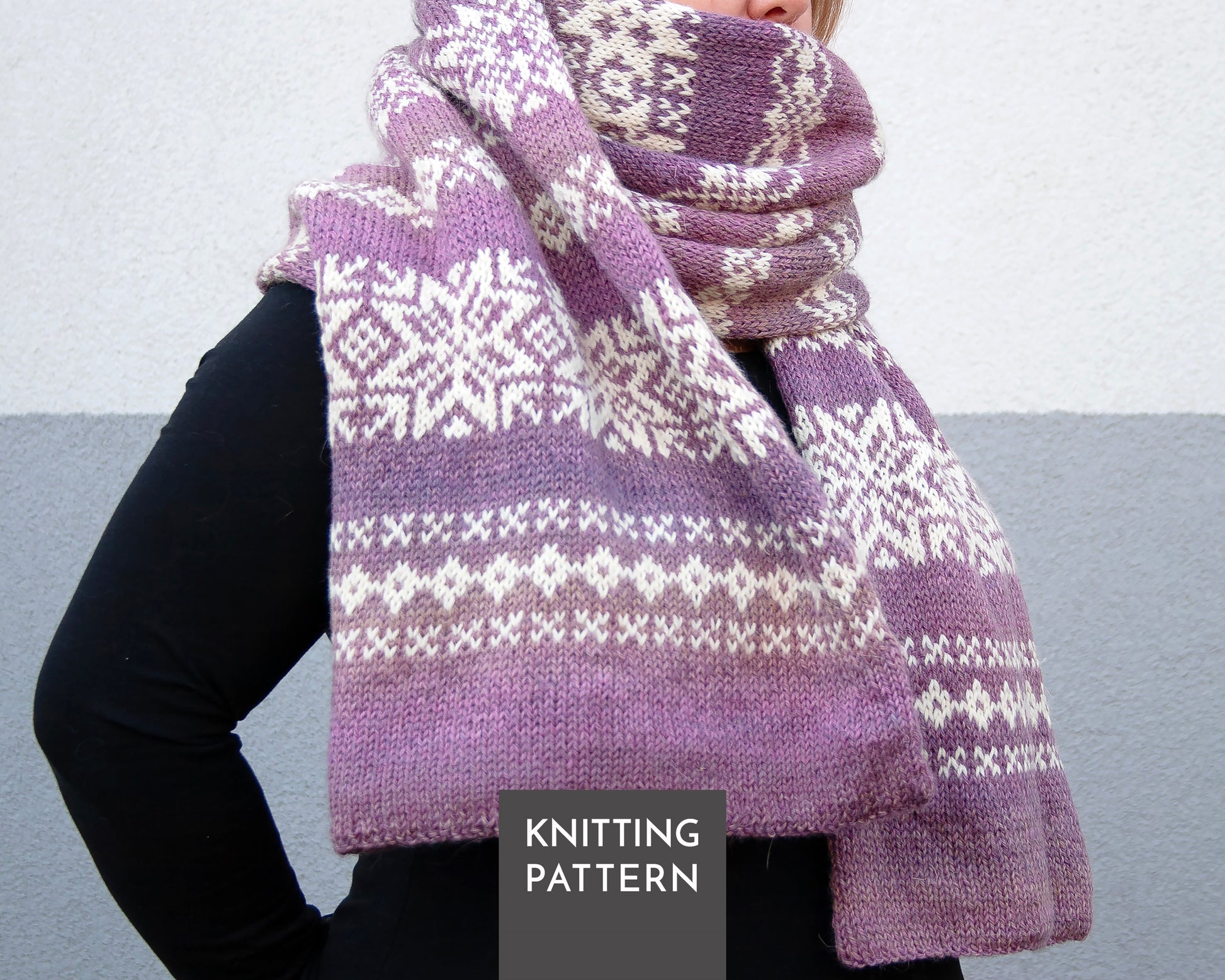A person wearing a knitted scarf with a purple and cream Nordic snowflake pattern