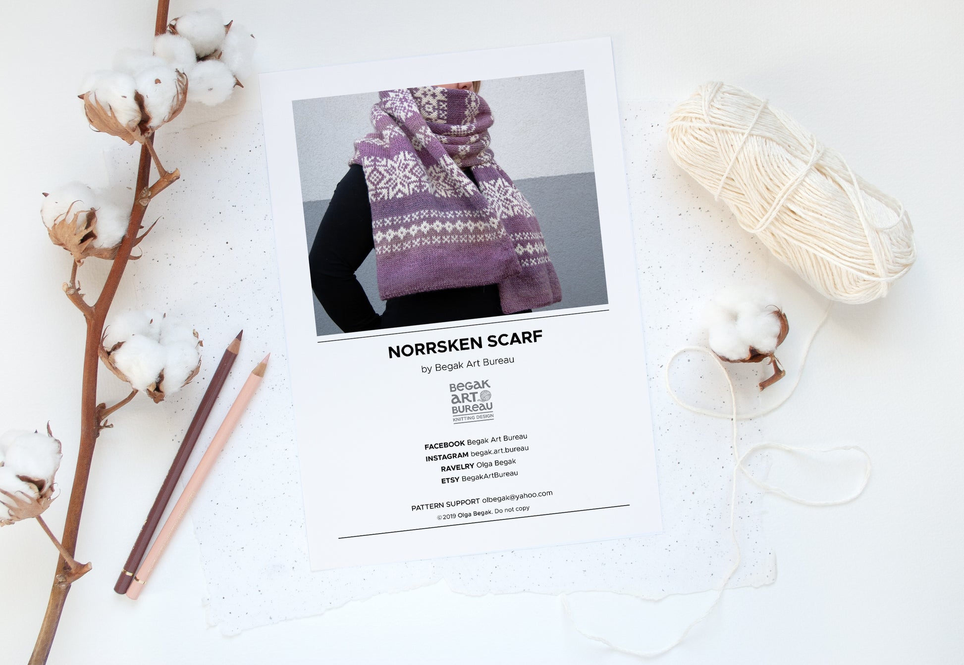 A flat-lay of a knitting pattern booklet for the 'Norrsken Scarf' by Olga Begak, featuring a photo of a purple and white patterned scarf.