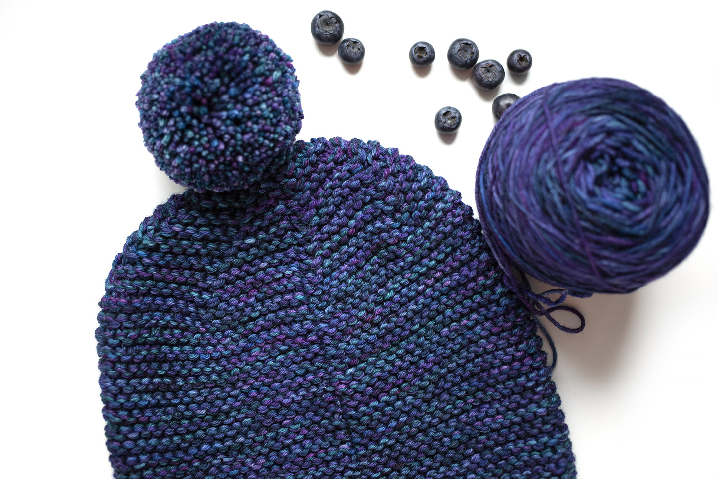 Back side of a blue and purple gradient wool garter stitch hand-knitted pom pom hat
